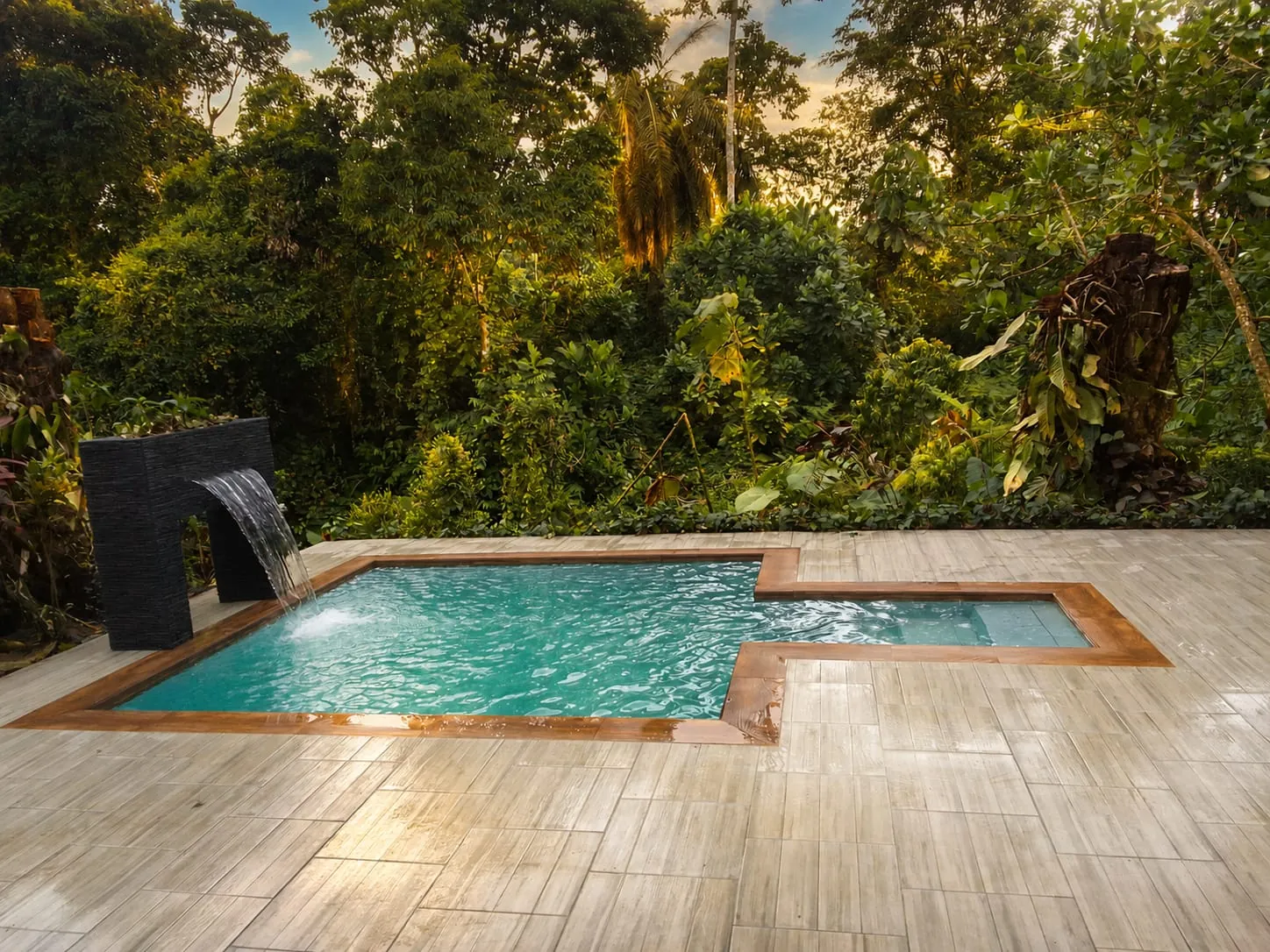 Piscina con cascada de piedra y borde de madera rodeada de vegetacion